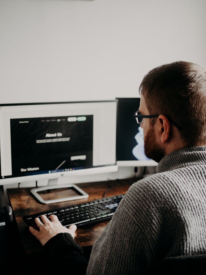 why-choose-us Man working on web design at home office setup with dual monitors.