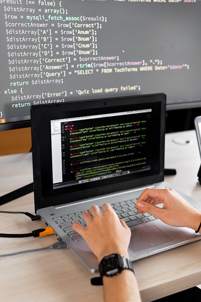 about-02 Person coding at a desk with laptop and external monitor showing programming code.